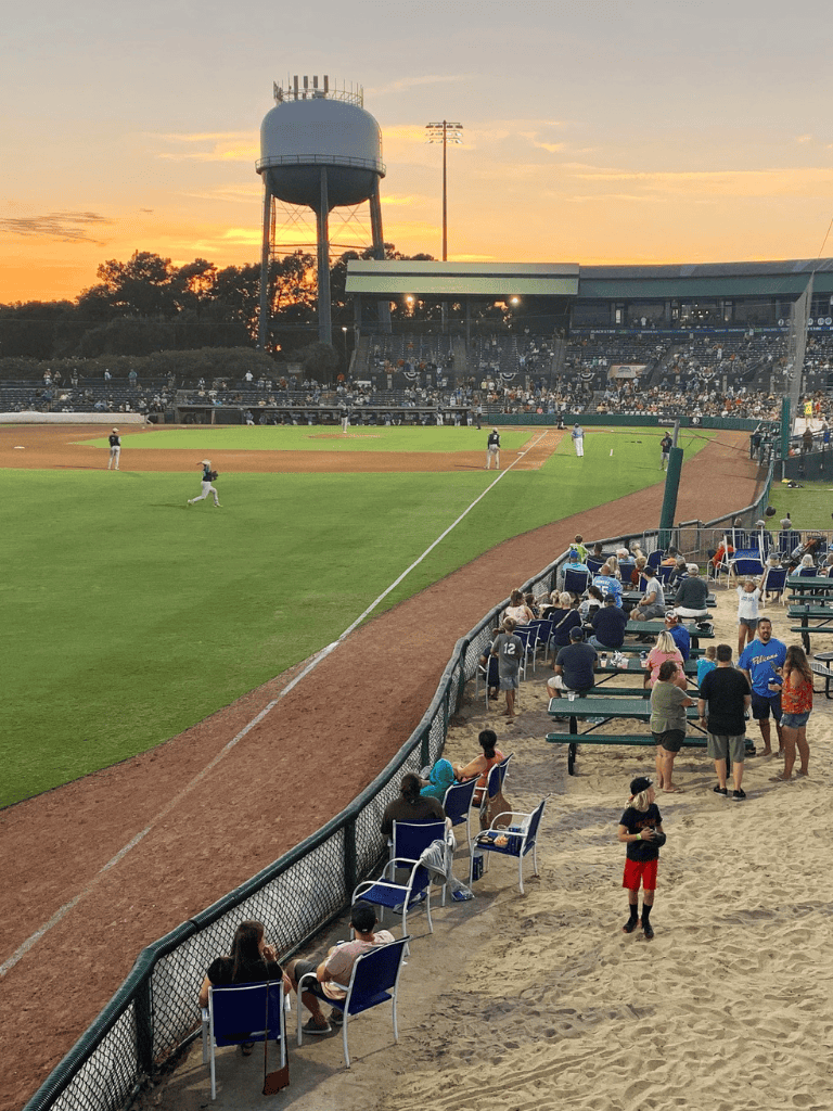 Amateur baseball game at sunset, fans enjoying the stadium atmosphere and the view.