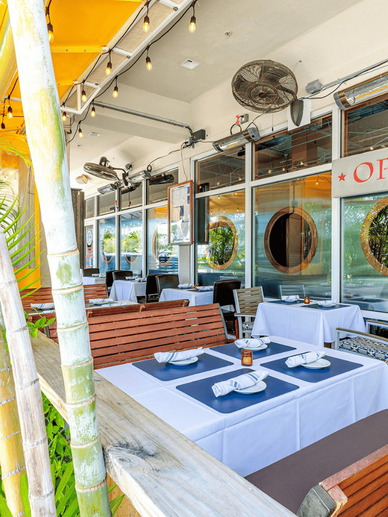 Chic outdoor restaurant dining with elegant table settings and tropical decor.