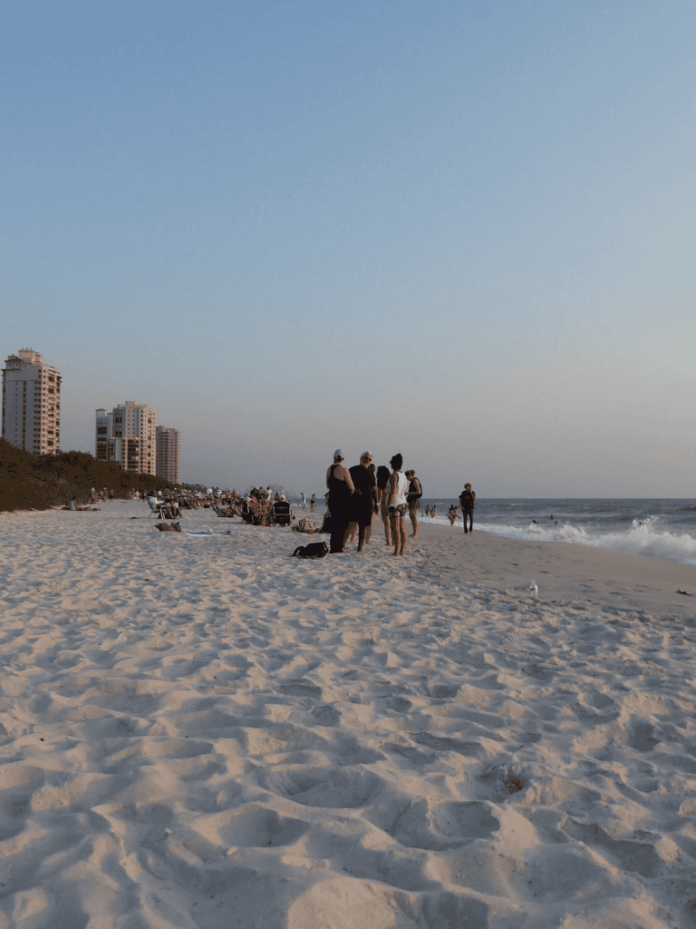People walking on the beach during sunset with city buildings in the background.