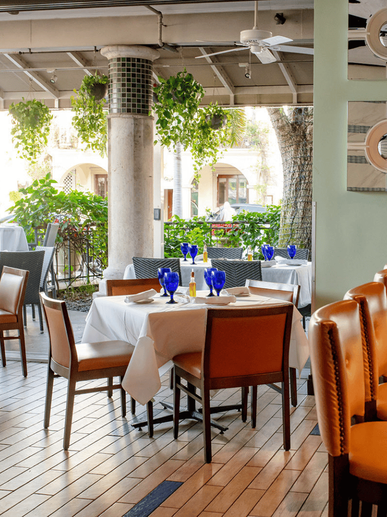 Outdoor restaurant patio with decorated tables and lush greenery.