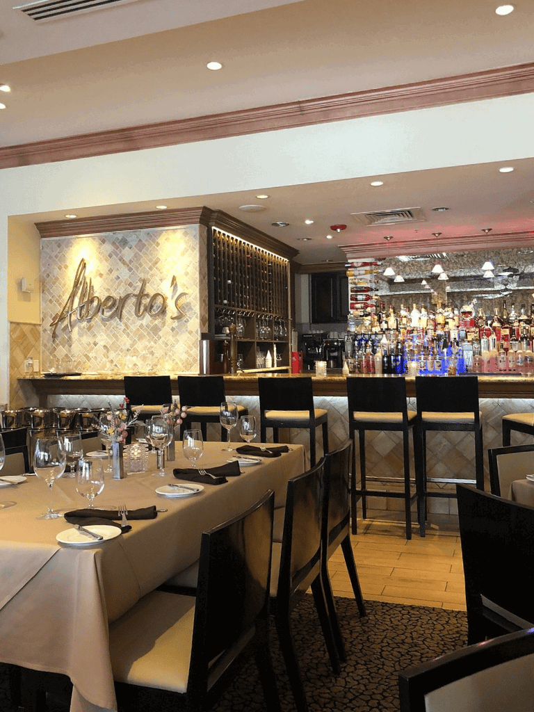 Outdoor dining area at Alberto's restaurant, featuring elegant table settings and a well-stocked bar.