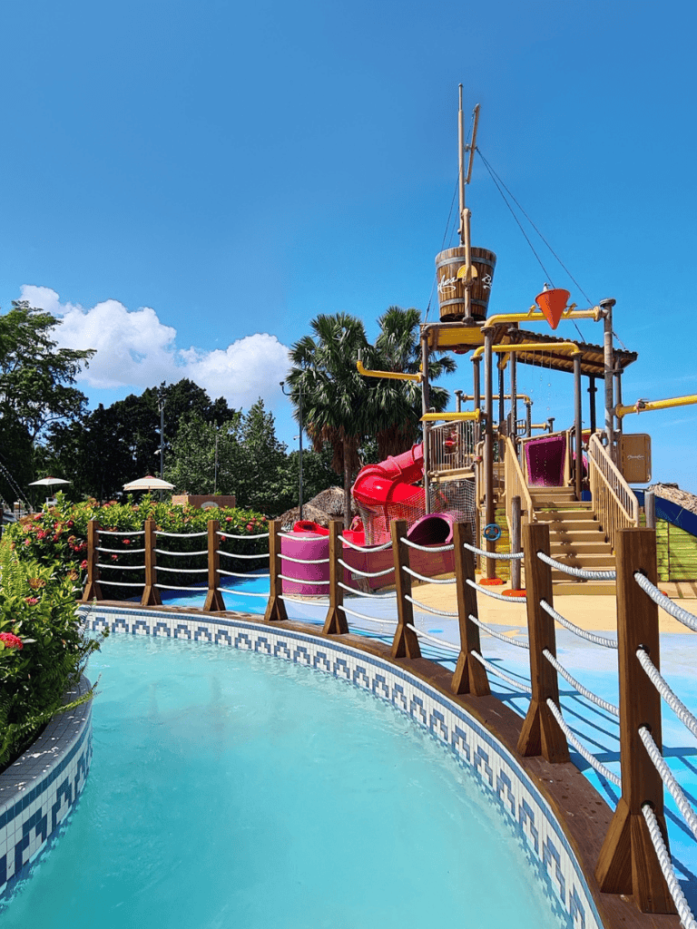 Colorful water park splash pad with slides, tropical trees, and bright blue sky for family fun.