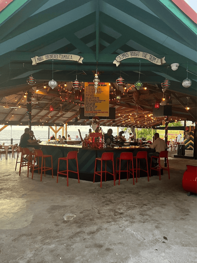 Bright seaside bar with colorful decor and guests enjoying drinks by the water.