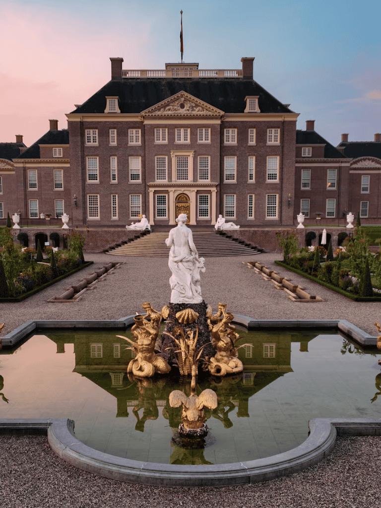 Elegant historic mansion with ornate fountain and landscaped gardens at sunset.