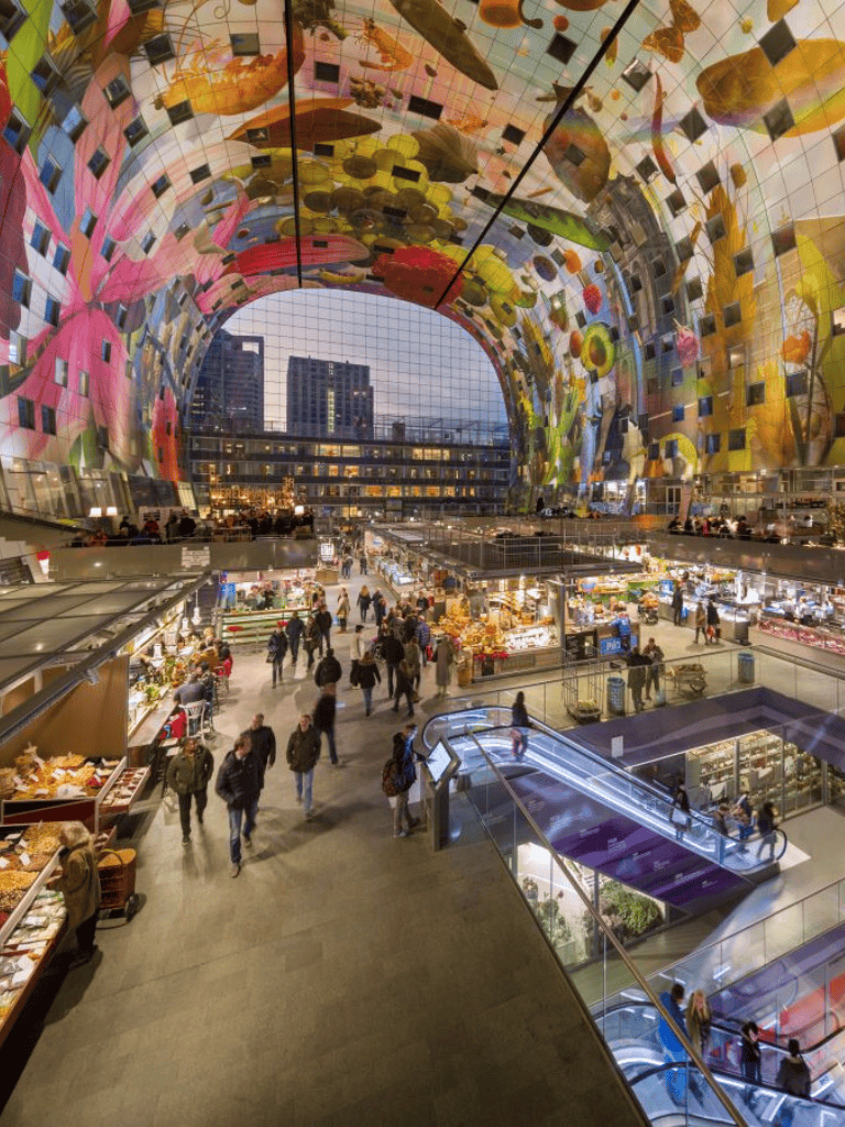 Colorful modern indoor marketplace with vibrant art installation ceiling, shoppers, and food vendors.