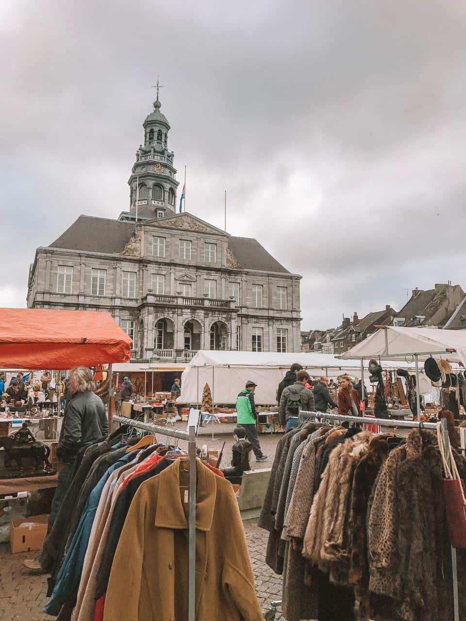 Colorful outdoor marketplace in front of historic European building, vibrant shopping scene, vintage clothing and local vendors.
