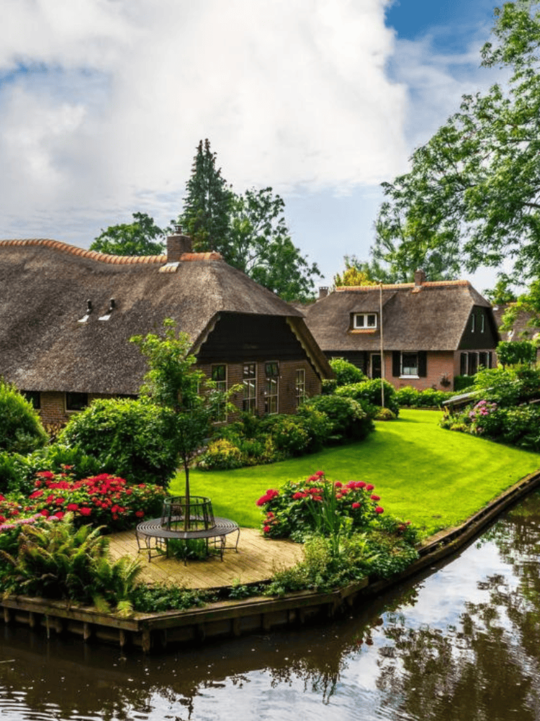 Charming traditional thatched cottages surrounded by lush garden and waterway, peaceful rural scenery.