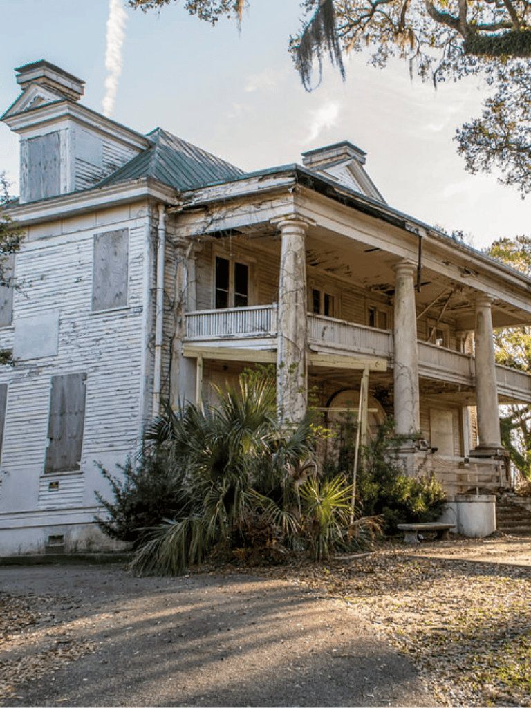 Dilapidated abandoned house with peeling paint and overgrown vegetation.