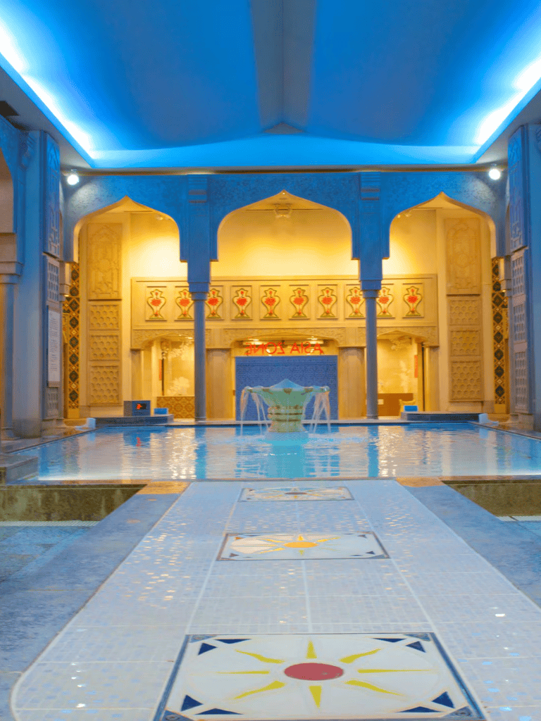Warm-toned indoor pool with traditional Indian architectural details and ambient lighting.