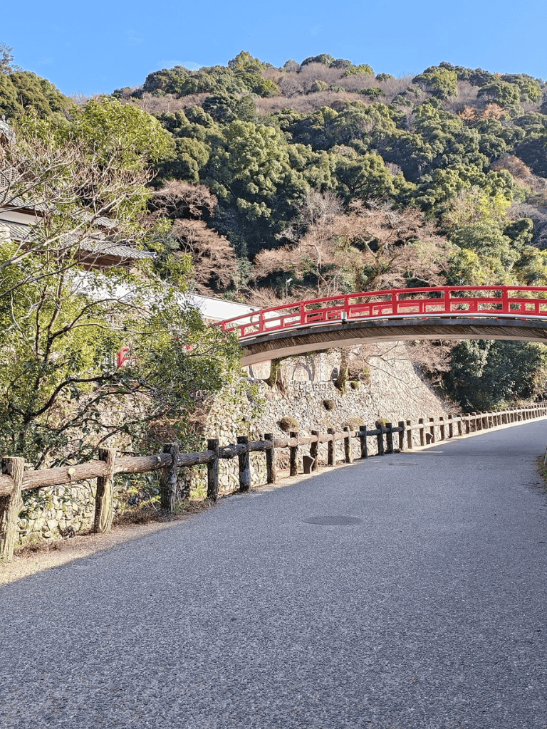 Quiet mountain path with traditional red bridge and lush green trees, scenic outdoor location.