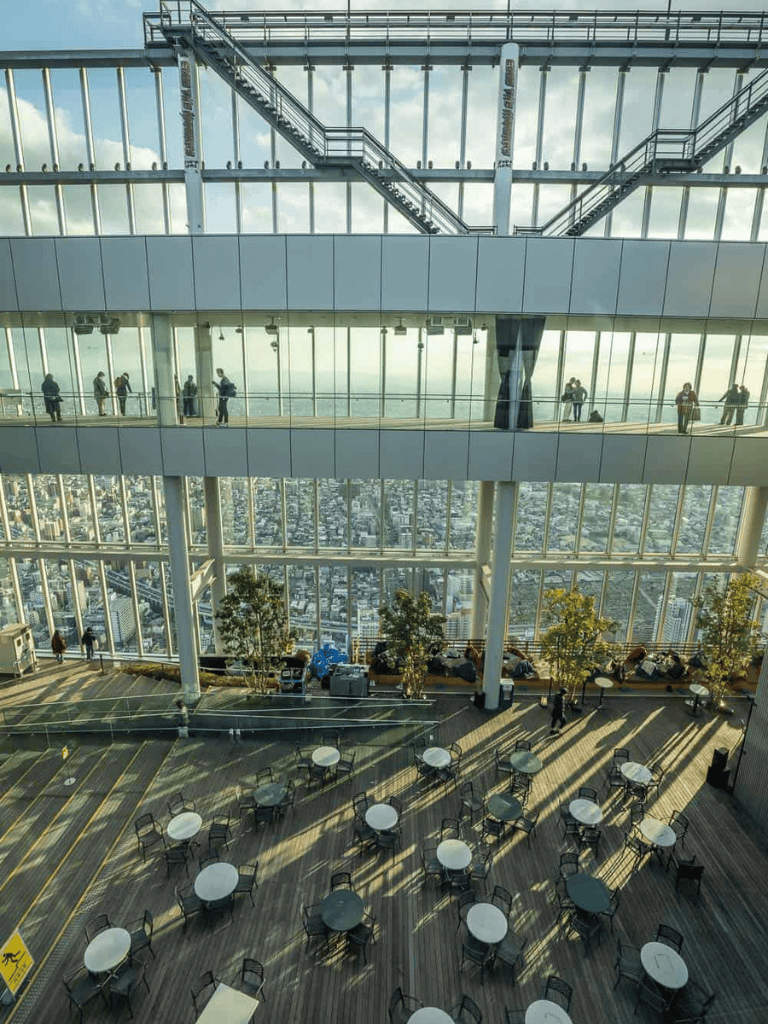 Aerial view of a modern skyscraper observation deck with glass walls and city skyline in the background.