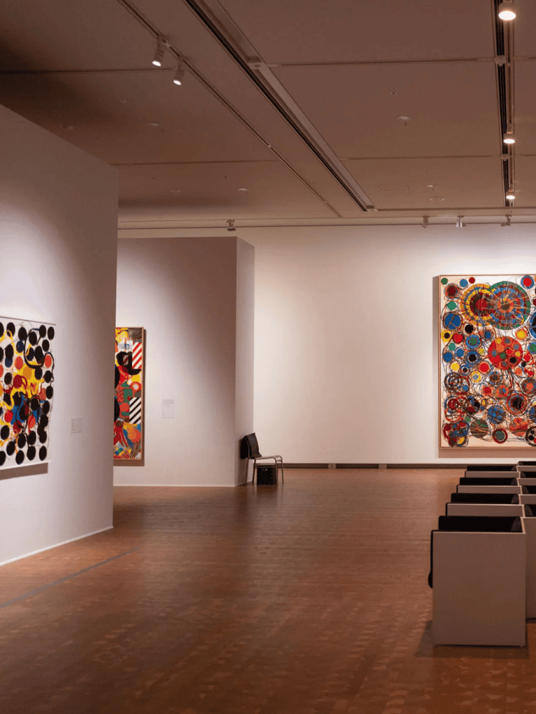 Vibrant abstract artwork displayed in a modern art gallery with warm lighting and wooden flooring.