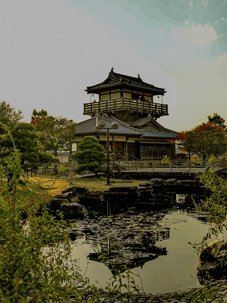 Ancient Japanese castle with traditional architecture and surrounding garden, reflects in pond.