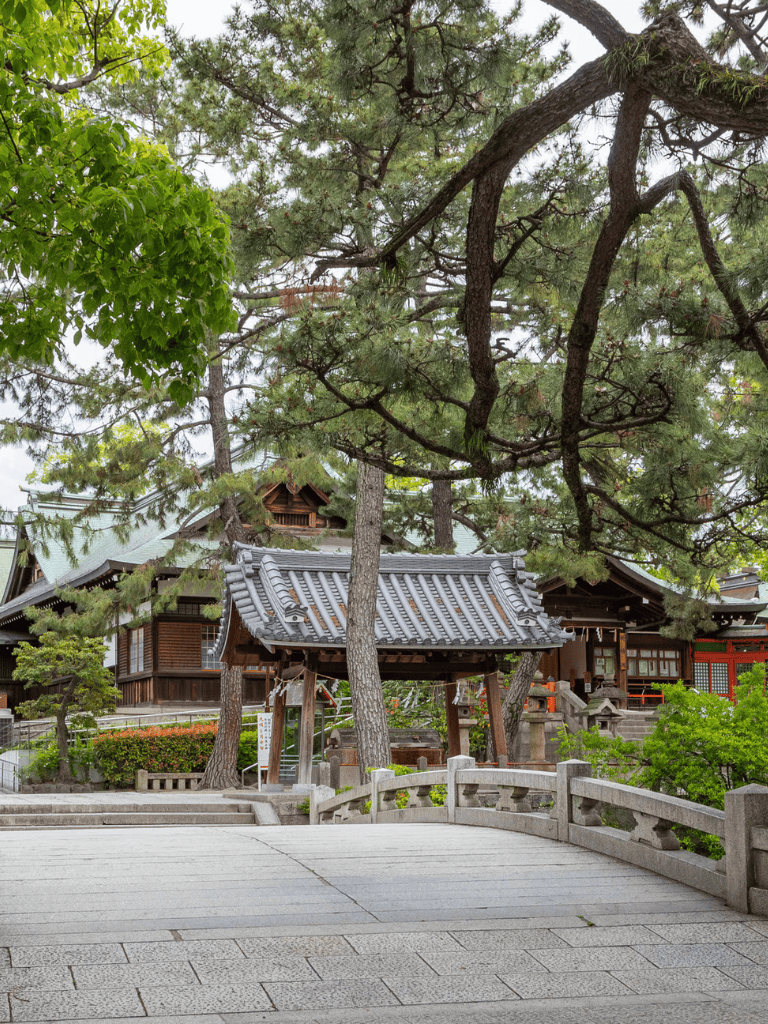 Serene traditional Japanese shrine nestled among green trees, with stone bridge in the foreground.