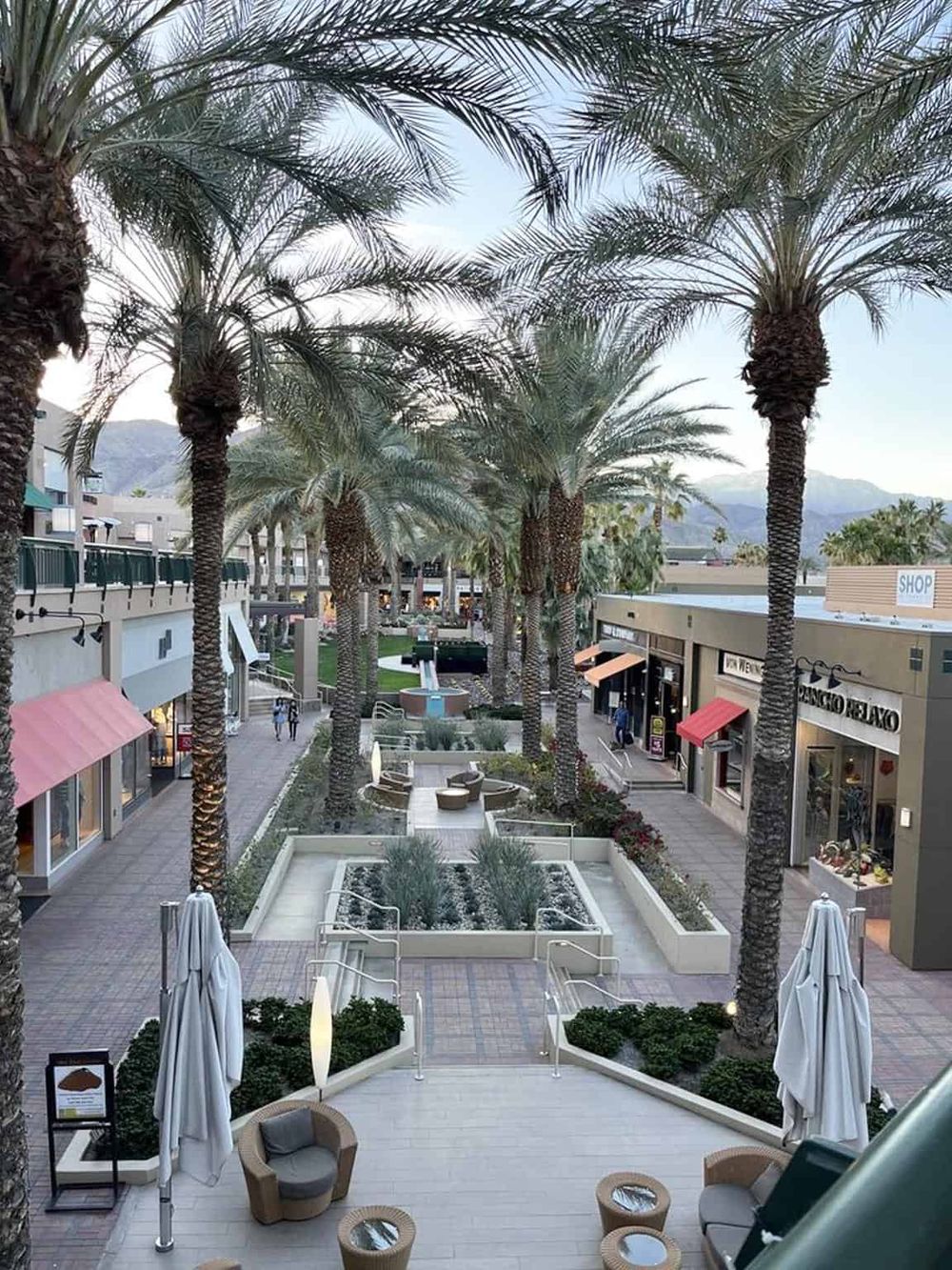 Vibrant outdoor shopping mall with palm trees, boutique stores, and inviting seating areas, perfect for leisurely strolling and shopping.