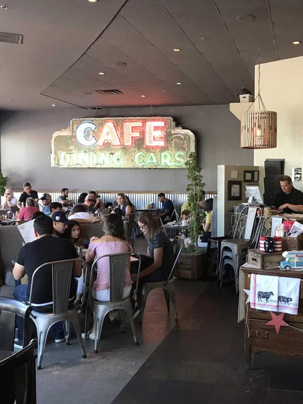 Cozy cafe dining area with neon "Café" sign and modern decor, inviting atmosphere for enjoying food and drinks.