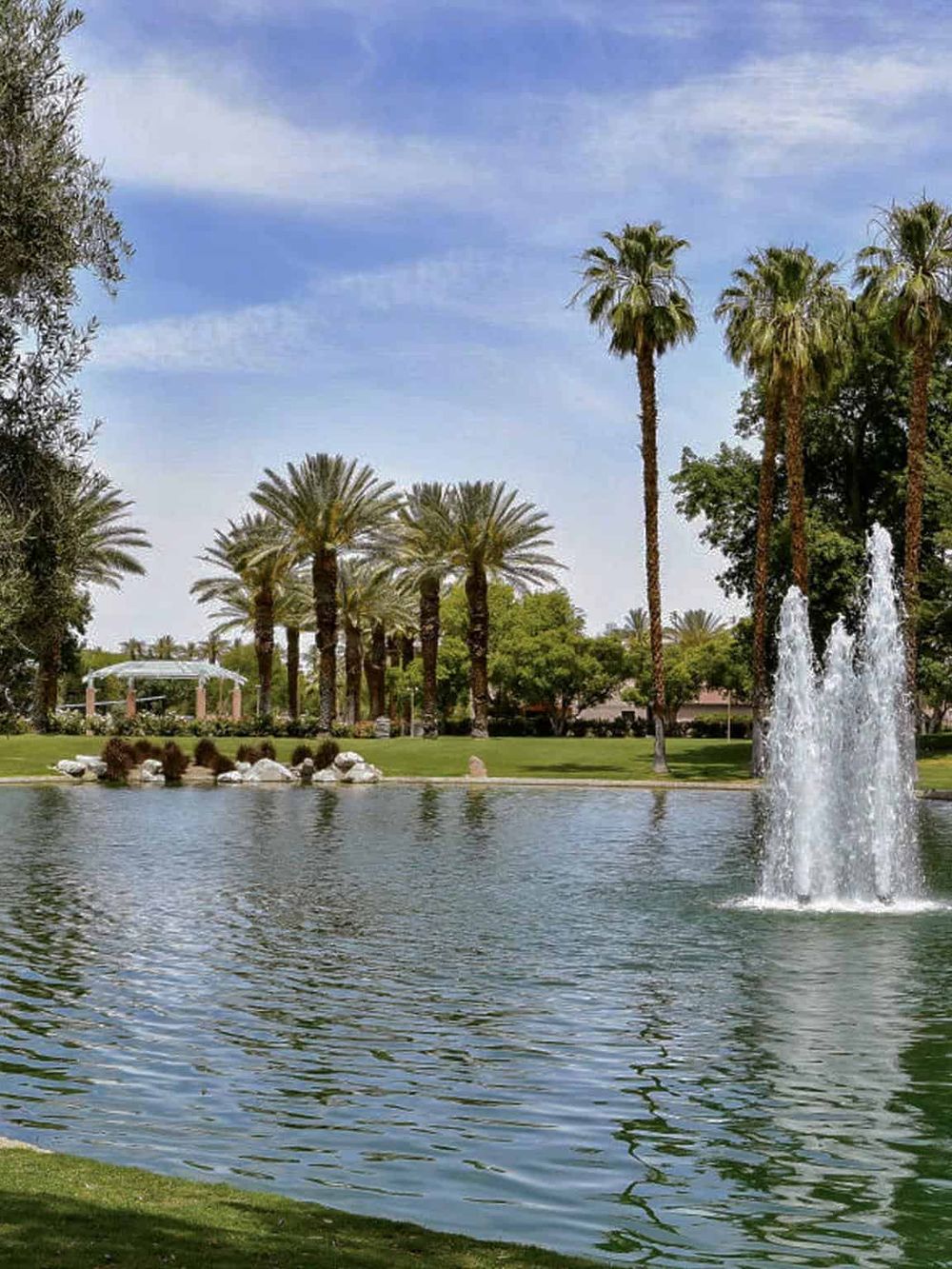 Lush park with pond, fountain, and tall palm trees, ideal for outdoor recreation and relaxation.