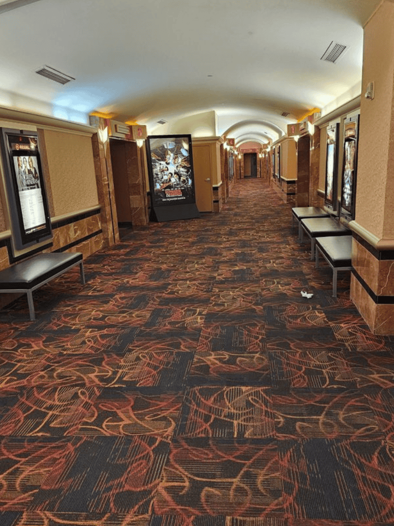 Empty theater lobby with vintage carpet, movie posters, and seating area, guiding visitors to film screenings.
