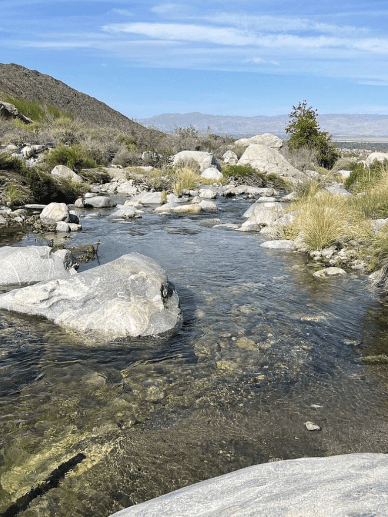 Peaceful desert stream with rocks and mountains in the background, perfect for outdoor adventures.
