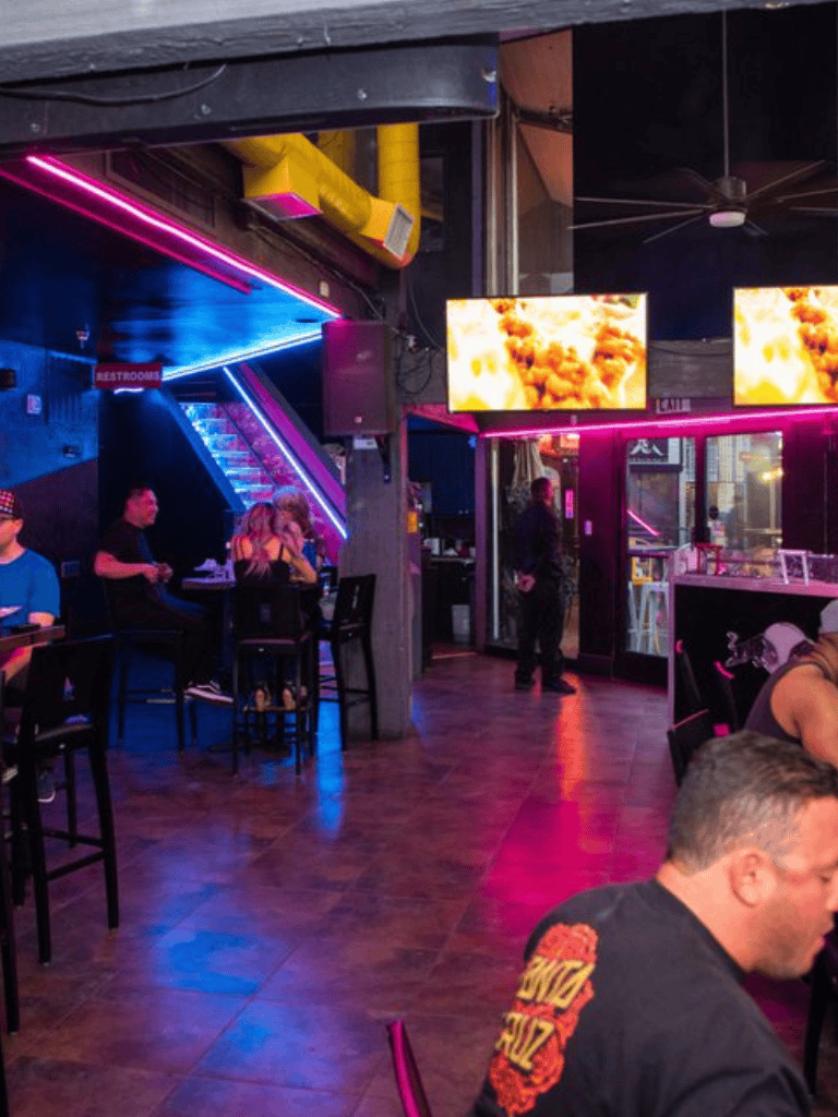 Vibrant neon-lit interior of a modern bar with customers enjoying drinks and entertainment.