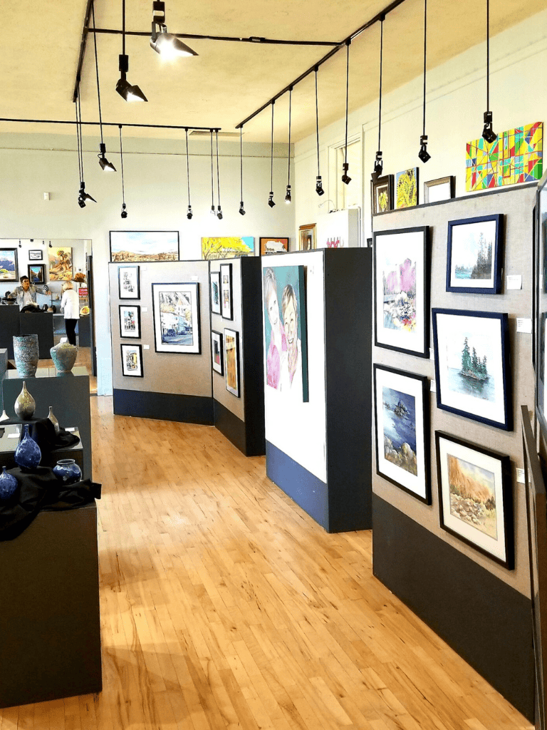 Colorful artwork displayed at an art gallery or art show with various paintings and ceramics.