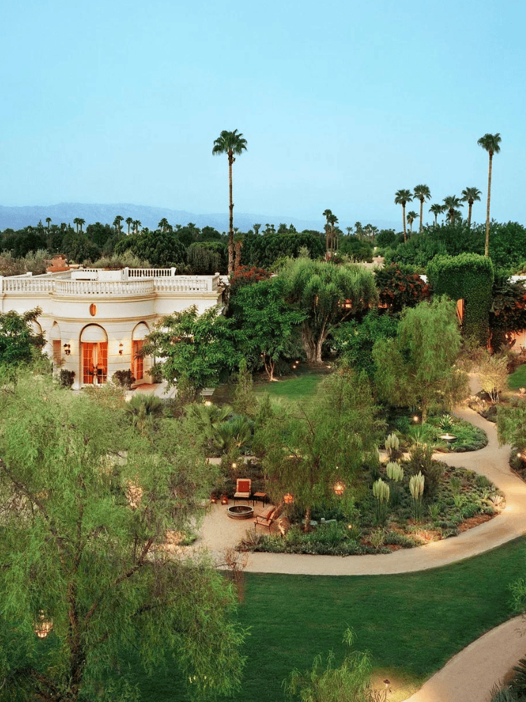 Lush desert landscape with palm trees, elegant architecture, and scenic view of mountains in the background.