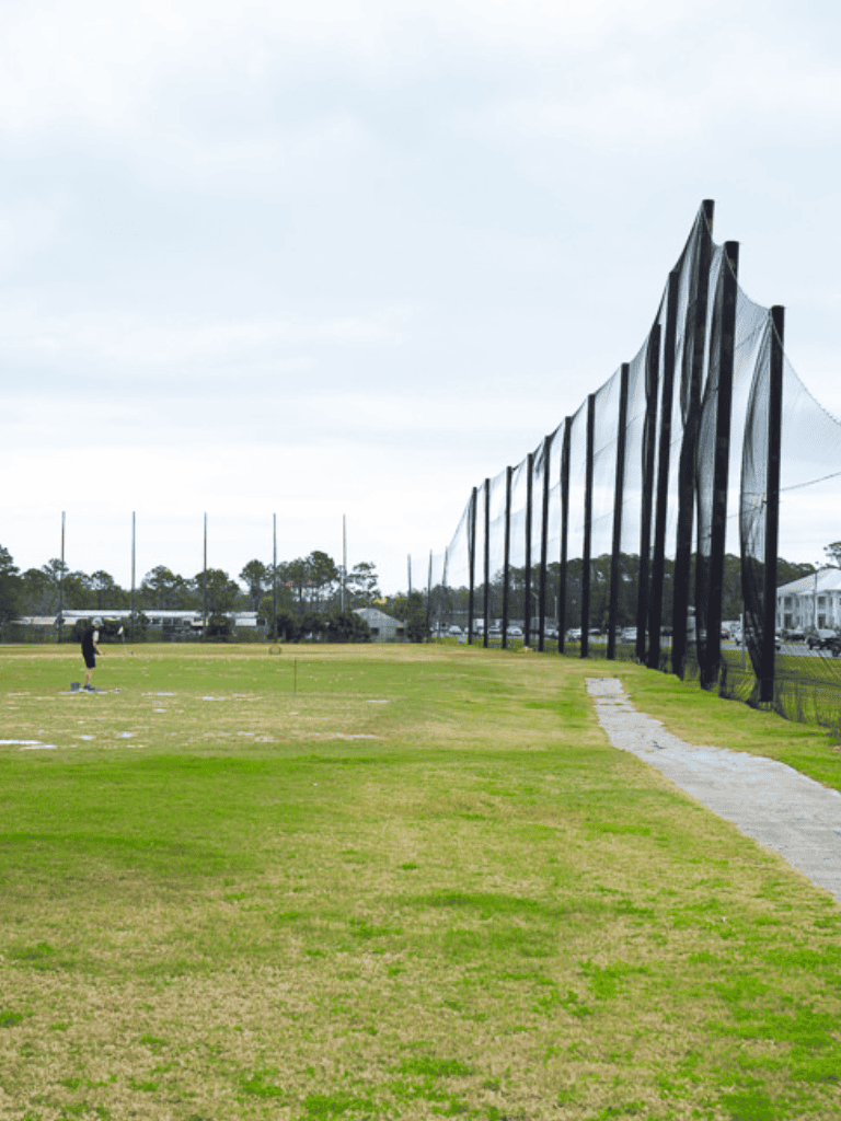 Driving range with golf netting at a sports complex, outdoor golf practice facility, hitting area with golfer.