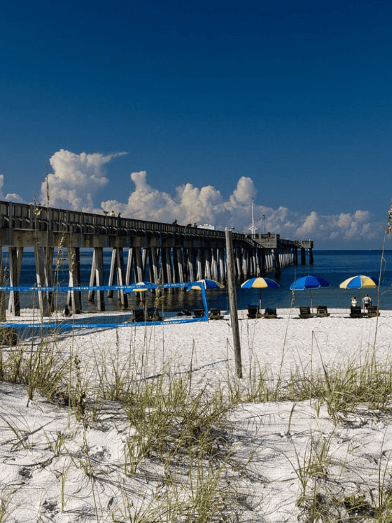 Calm beach scene with pier, umbrellas, and volleyball net at QuestForDirections.