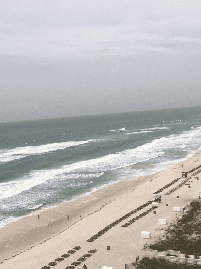 Cloudy beach scene with waves and empty lounge chairs, perfect for seaside relaxation.