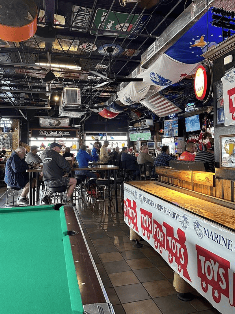 Bright interior of a lively bar or sports pub with patrons watching a game on TV and patriotic decorations overhead.