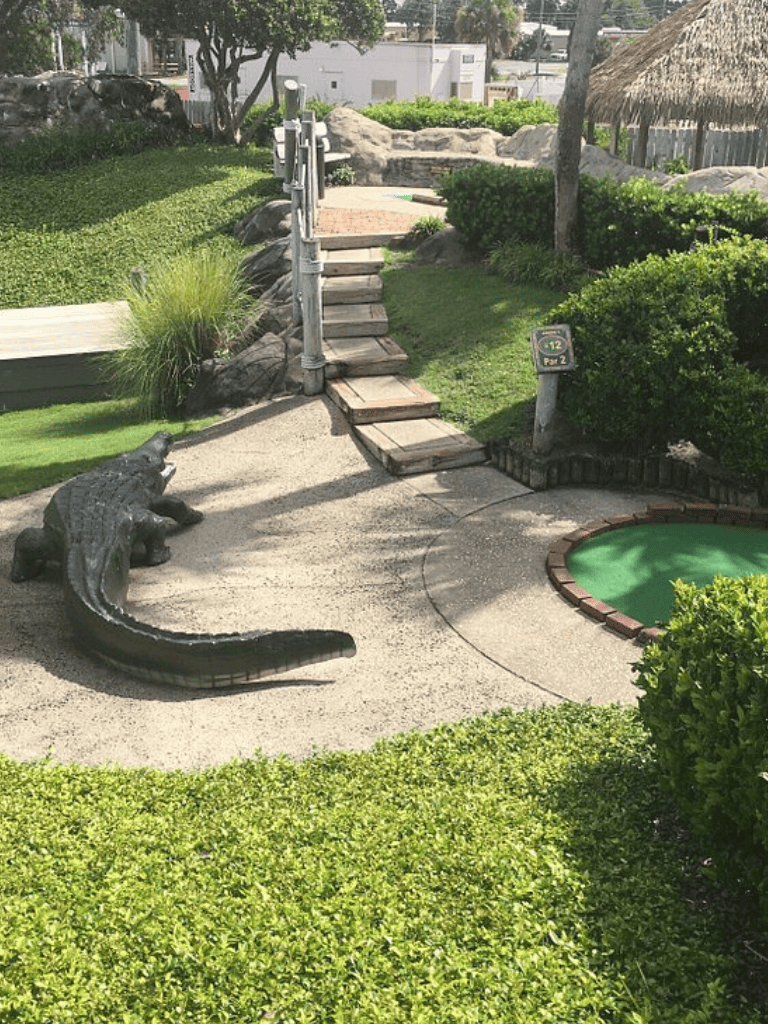 Lush backyard mini-golf course with crocodile statue and scenic landscaping.