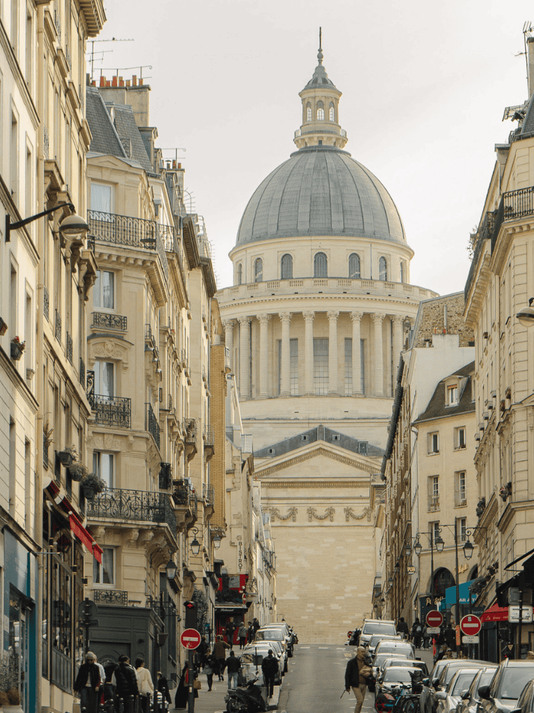 Historic Paris street view with the Panthéon in the background, showcasing classic French architecture and lively urban atmosphere.