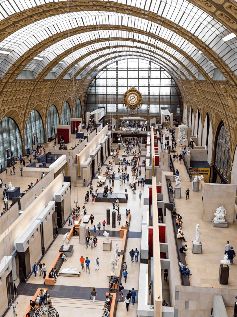 Elegant train station interior with high arched glass ceiling and busy crowds, featuring historical architecture and modern retail spaces.