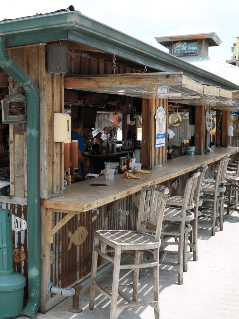 Rustic oceanfront beach bar with weathered wood stools and bar counter, offering refreshing drinks and seaside views.