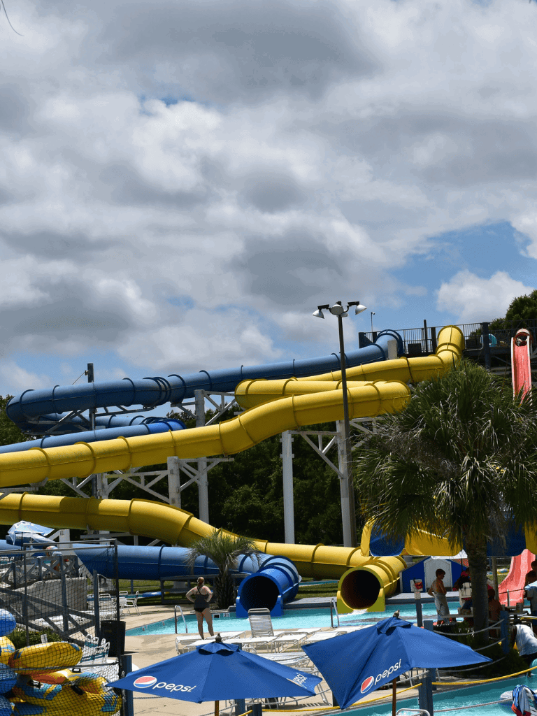 Colorful water slides at a water park with umbrellas and palm trees, perfect for family fun and summer relaxation.