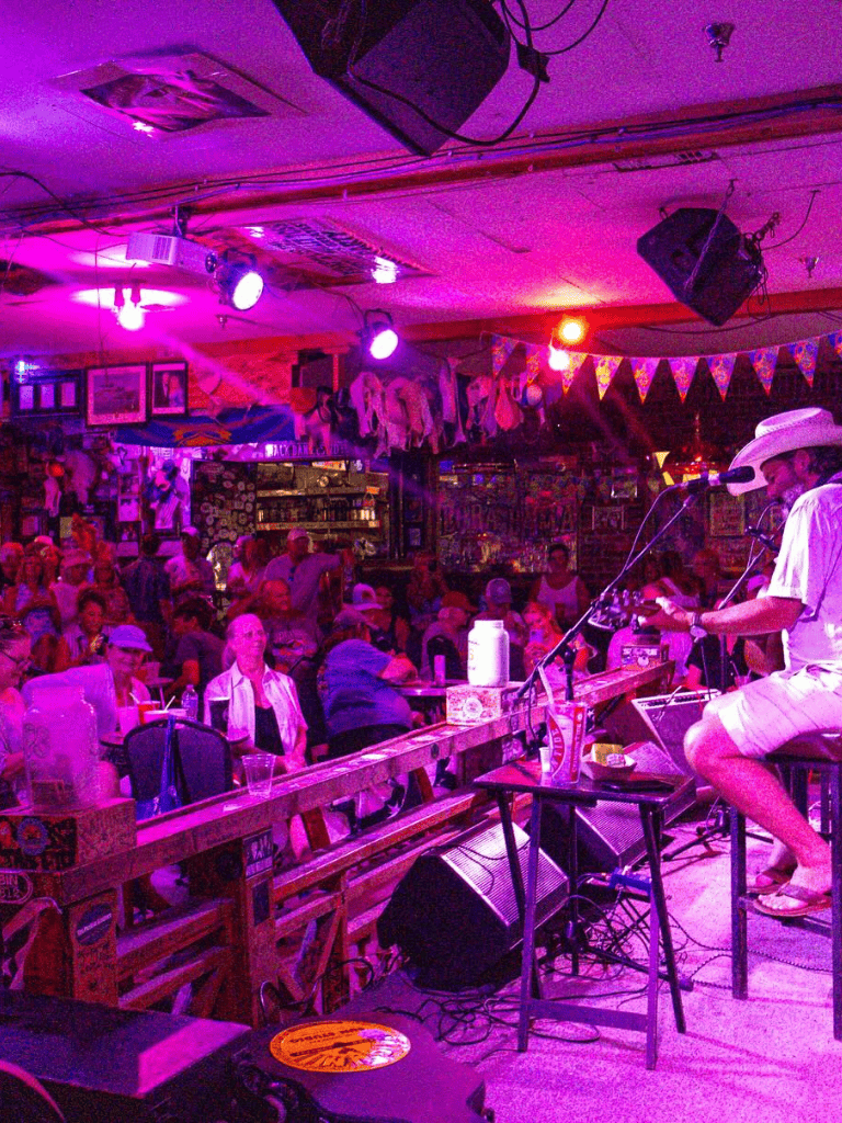 Live country music performance at a vibrant bar or restaurant with colorful lighting and audience engagement.