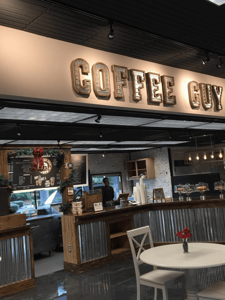 Warm cozy coffee shop interior with "Coffee Guy" sign, festive decor, and inviting seating area.