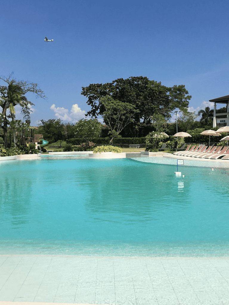 Relaxing swimming pool area at Quest for Directions resort with lush greenery and clear blue sky.