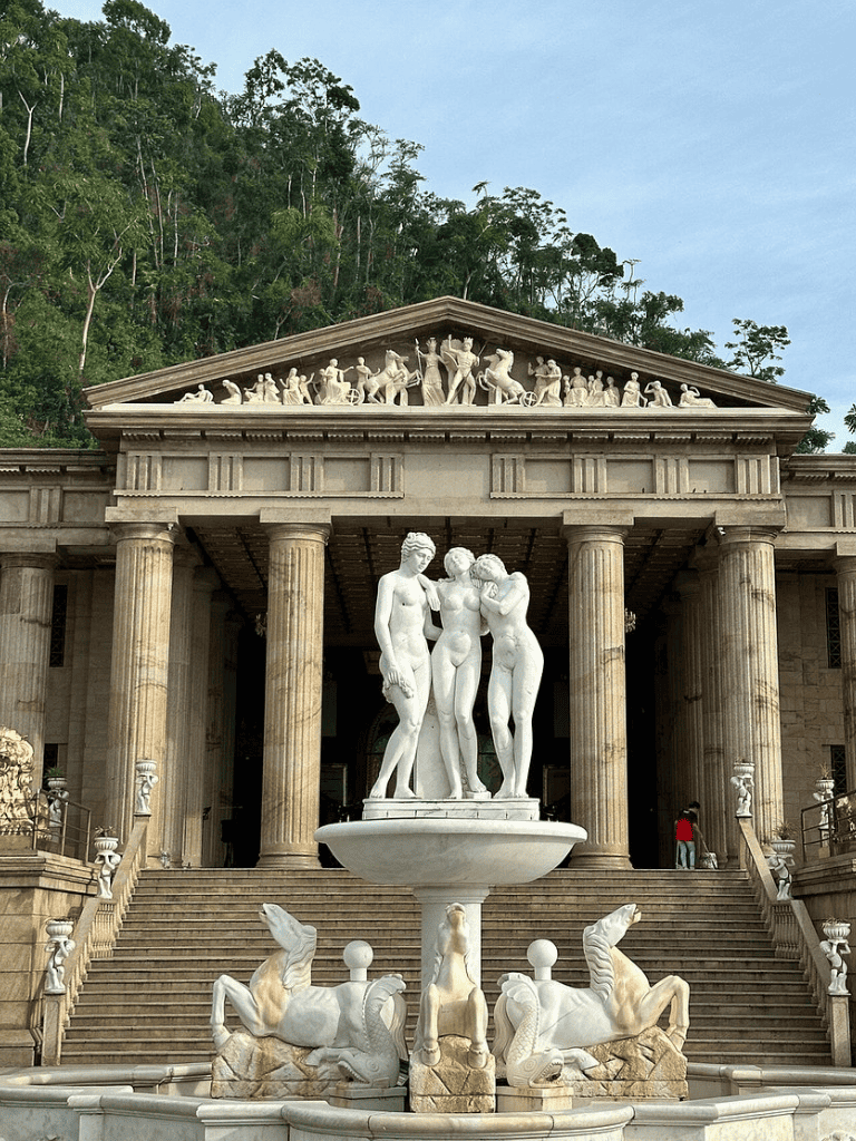 Eiffel Tower replica with classical statues in a lush, green setting, showcasing historical architecture and sculptures.