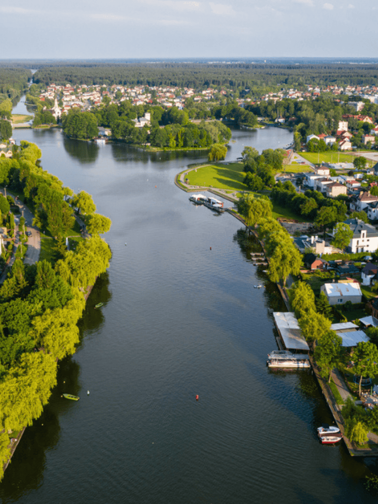 Serene river landscape with lush green trees, residential homes, and boats on the water.