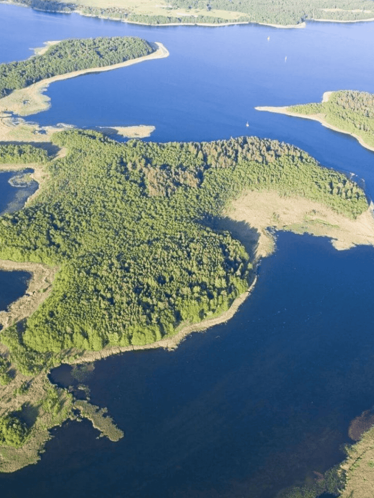 Lush green forested island with surrounding calm blue water, aerial view of nature landscape destination.