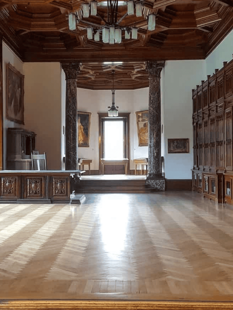 Elegant historic interior with wooden accents and classic decor, featuring large windows and ornate woodwork.