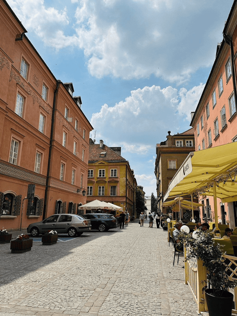 Colorful European street with outdoor cafes and historic buildings under a bright blue sky.