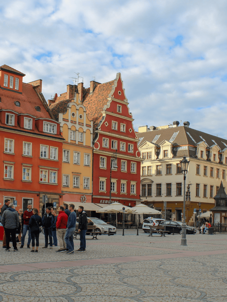 Colorful European buildings in a lively city square with tourists and cafes, showcasing travel and city exploration.