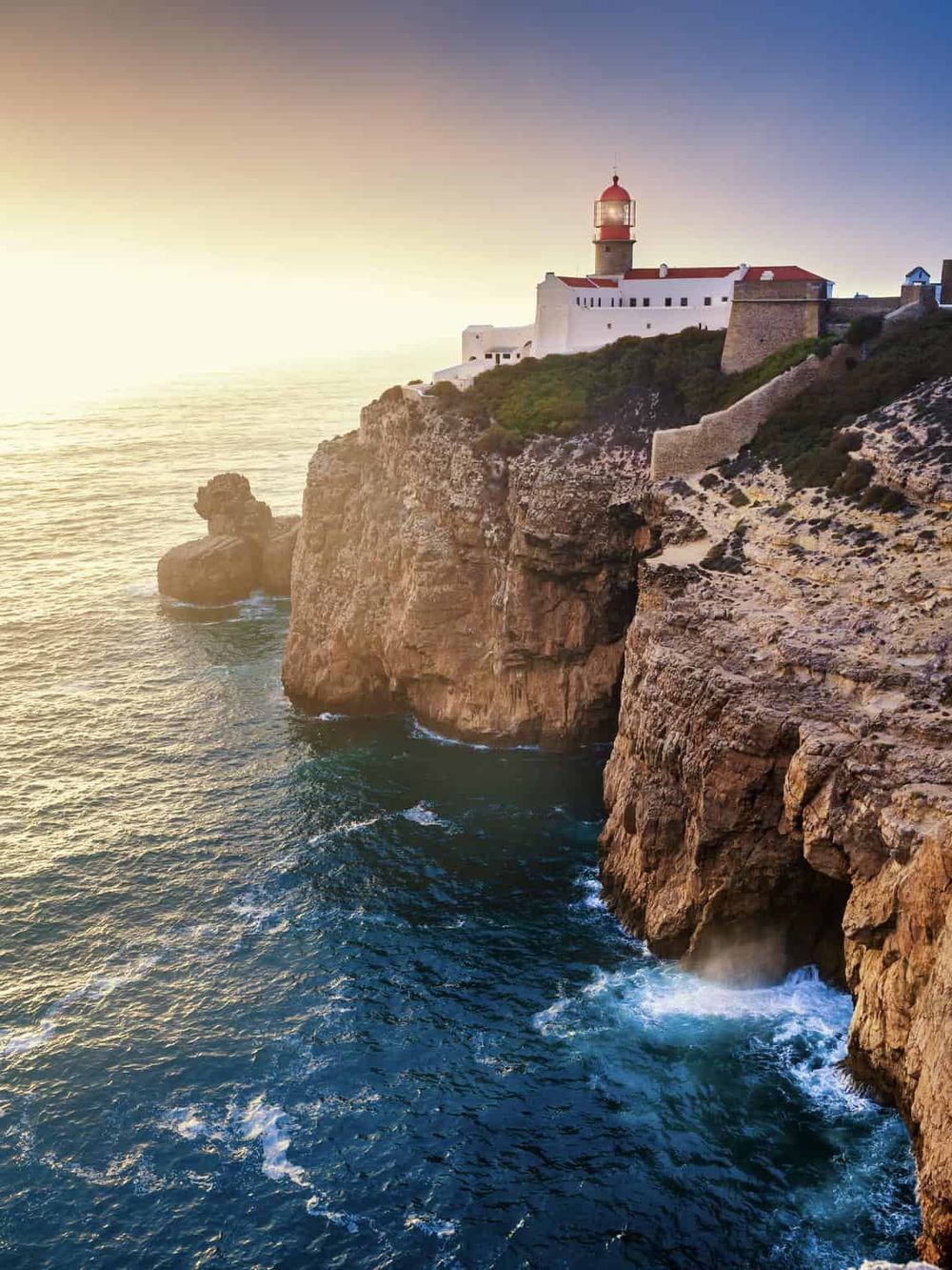 Lighthouse on rugged coastal cliffs during sunset, scenic view of the ocean and coastline.