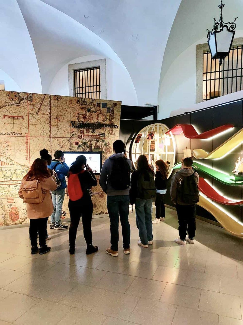 Colorful museum exhibit showcasing historical maps with visitors engaging with interactive displays.