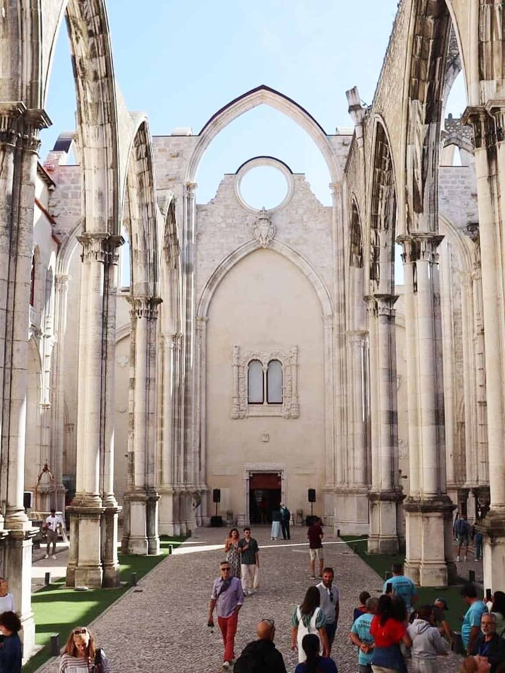 Ruins of a historic cathedral with Gothic architecture, open sky, and visitors exploring the site.
