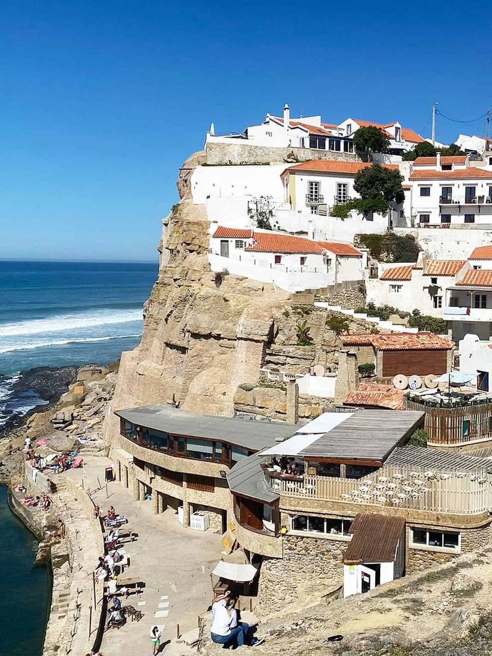 Clifftop white houses with red-tiled roofs overlooking the ocean, iconic in coastal Portugal.