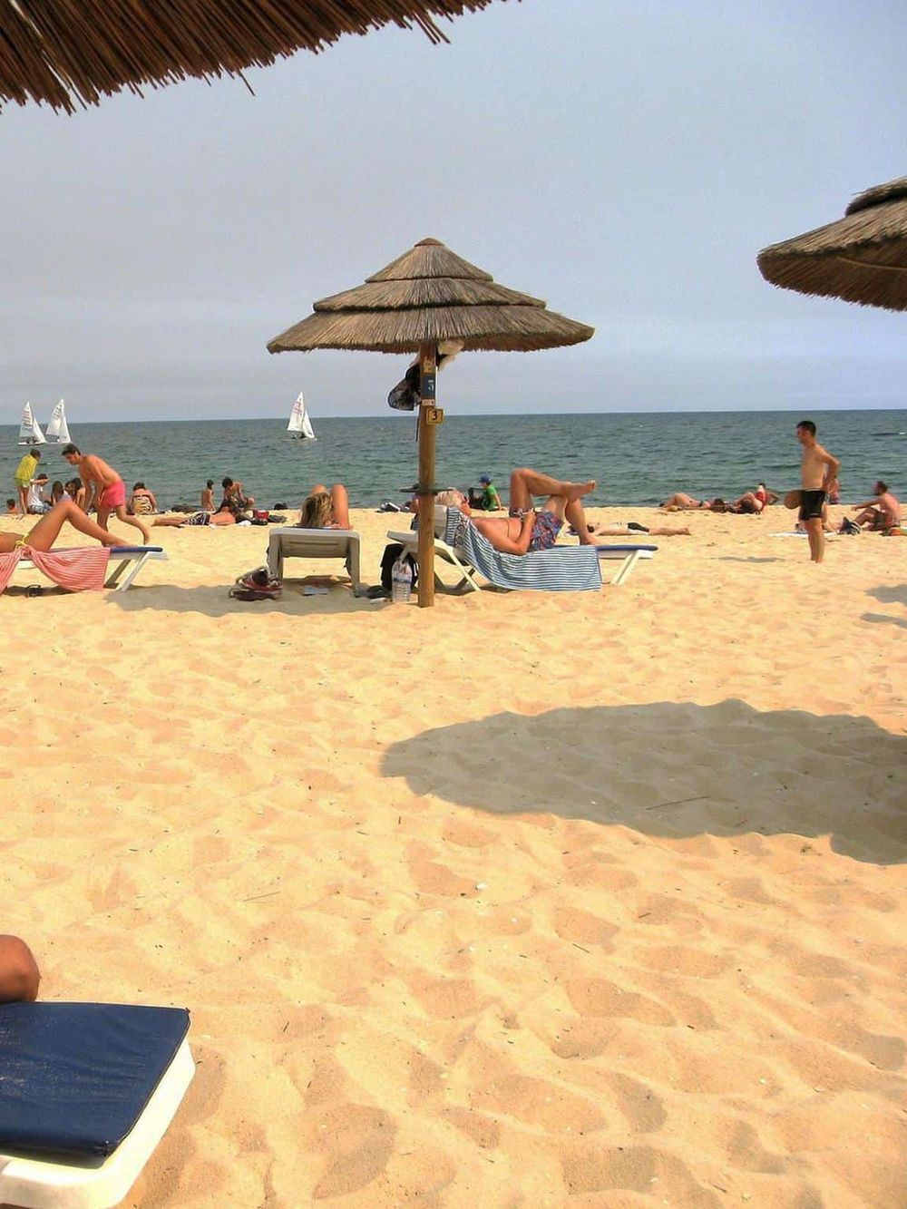 Vibrant beach scene with umbrellas, sunbathers, and sailboats on the ocean, ideal for seaside vacation and outdoor relaxation.