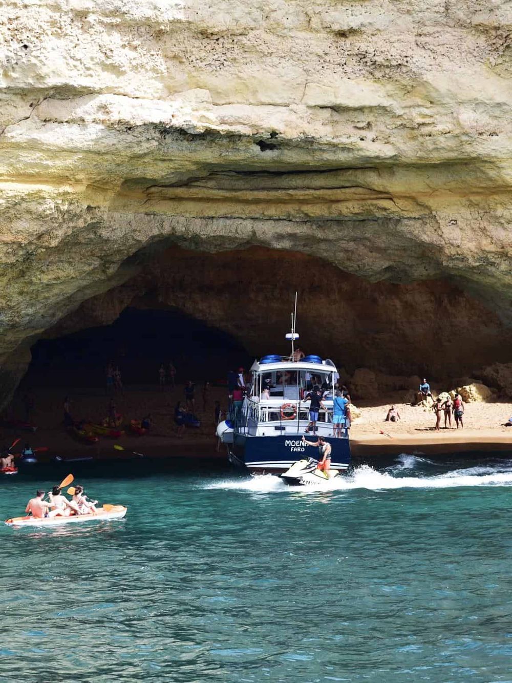 Vibrant boat and jet ski activity at the scenic coastal cave with tourists enjoying water adventures.